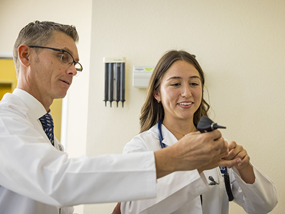 Brian S. Lauf helping a Physician Assistant use a otoscope on a patient in a clinical setting
