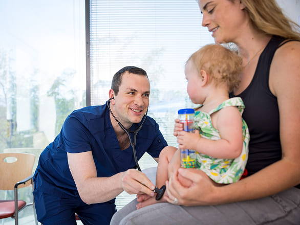 A pediatric doctor smiles at a patient being held by her mother