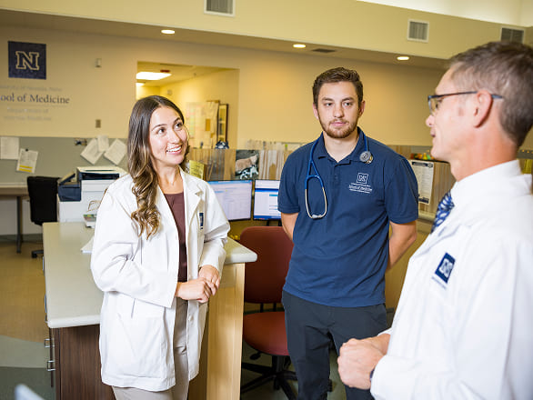 Two physician assistant students talk with a doctor in a clinic