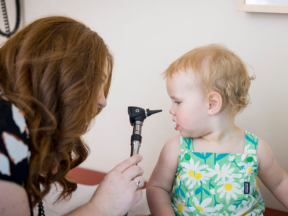 A doctor leans in to examine a baby's ears with a scope, but the baby is facing her, looking down the center of the scope