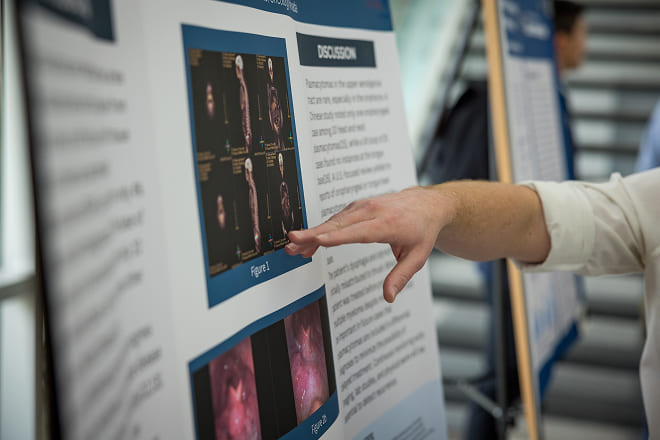 A hand points to information on a student research poster
