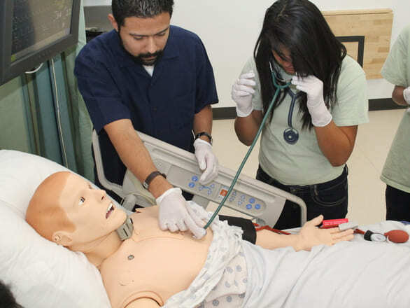 Medical instructor guiding a medical student using a stethoscope on a patient manikin during a simulation