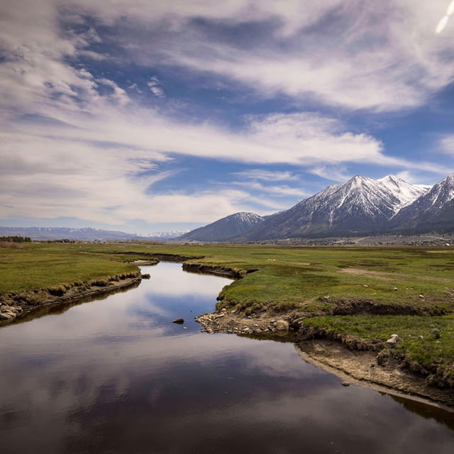 Rural landscape with a river, open fields, and mountains in the distance.