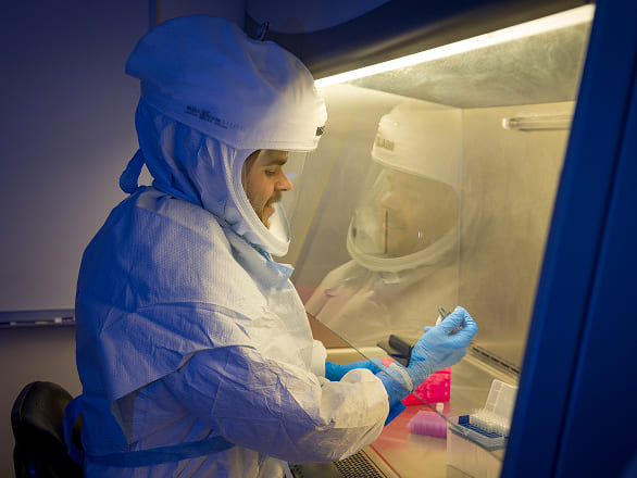 A researcher wearing a full coverage biohazard suit works under a ventilation hood