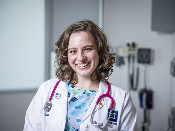 A medical student in their white coat smiling.