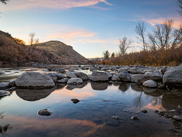 Riverbed with rocks and sunset reflection.