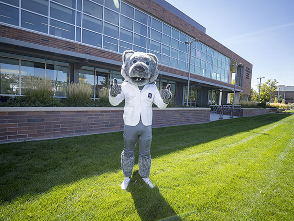 Wolfie mascot in a white coat outside of Pennington Health Sciences building.