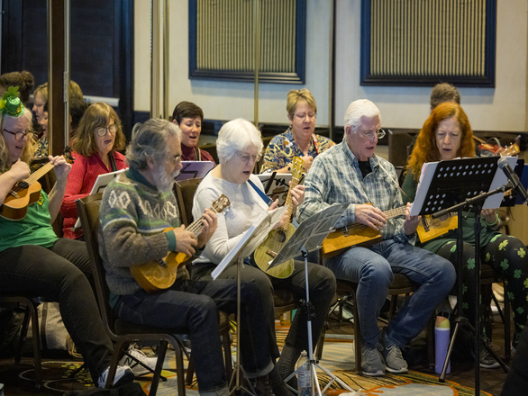 A group of elderly people playing ukuleles and singing together in a room.