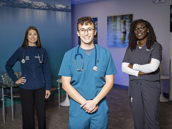 Three residents in scrubs standing in a clinical waiting room.