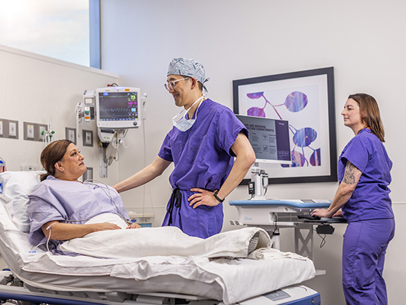 A surgeon in a hospital room talking with a patient in a bed.