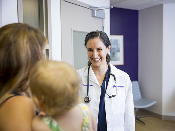 A pediatrician in a white coat talking to a mother and their child.
