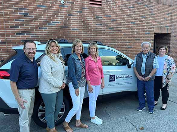 A group of people standing in front of a donated vehicle that had the Sanford Center for Aging logo