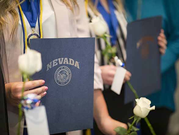 graduates holding certificates and roses at a ceremony