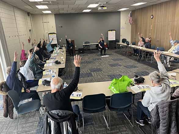 A group of people sitting around a table with hands raised