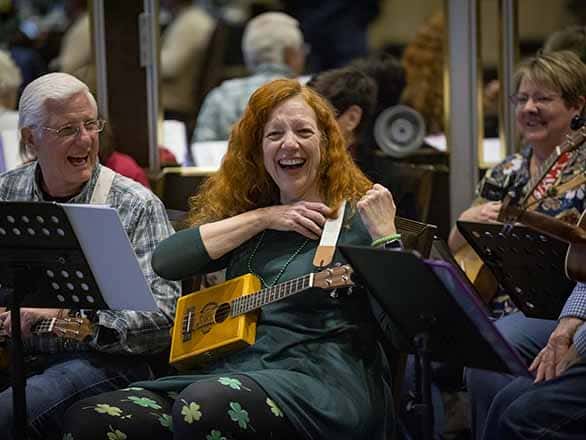 Three people smiling while playing ukuleles