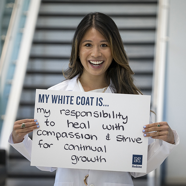 Cat Ung holding a sign that reads, "My White Coat is... my responsibility to heal with compassion and strive for continual growth."