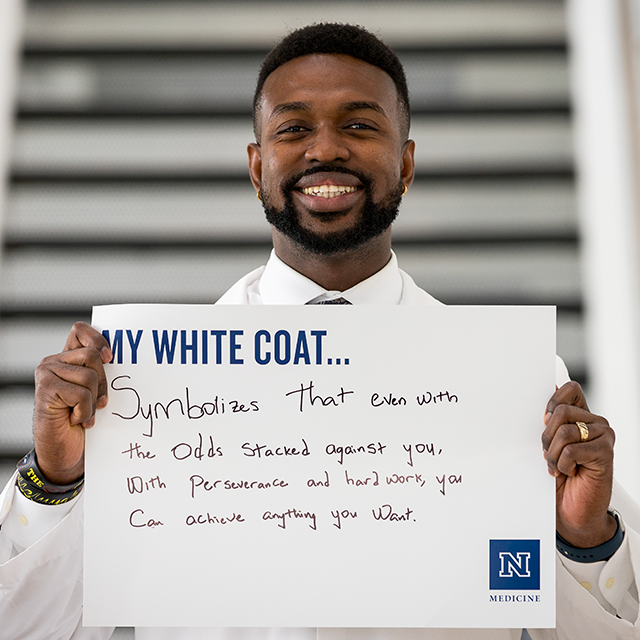 Olawale Akinyemi holding up a sign that reads, "My White Coat... Symbolizes that even with the odds stacked against you, with perseverance and hardwork, you can achieve anything you want."