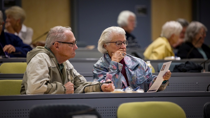 An older couple sitting together in a lecture hall, attentively reading a UNR Med pamphlet
