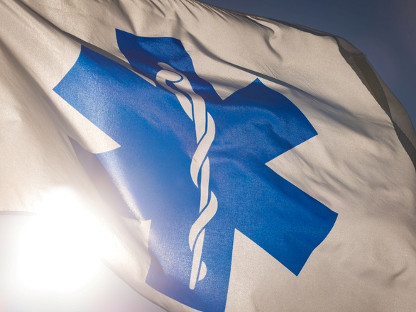 A medical flag that has a Star of Life symbol flutters in the wind against a clear blue sky