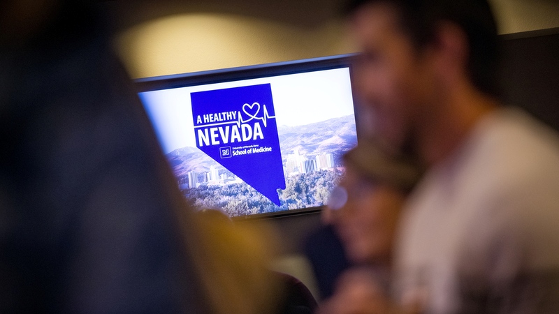 An audience sitting with the Healthy Nevada UNR Med logo displayed on a TV screen in the background 