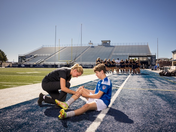 A medical student examines an athlete’s injured leg on a sports field