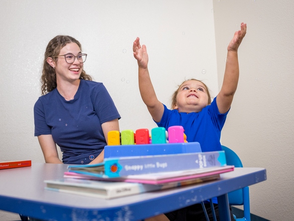 A Speech Pathology and Audiology student working with a child patient seated at a table, with the child attempting to pop a bubble