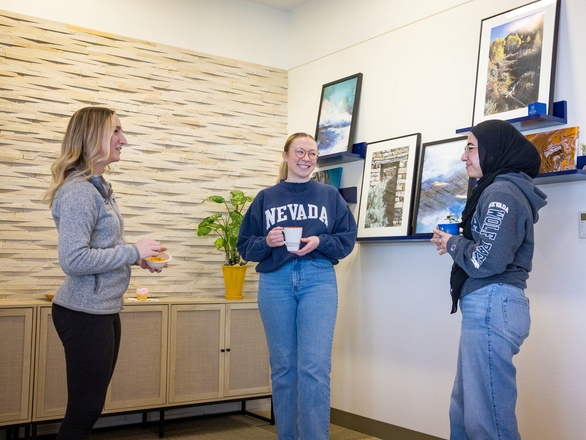 Faculty staff and two students stand side by side in front of a wall filled with photographs, enjoying a moment together.