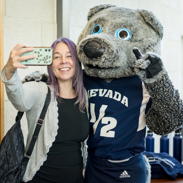 A faculty member smiles while taking a selfie with Wolfie Jr., one of UNR’s mascots.