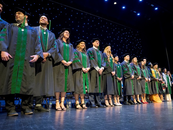 A group of medical graduates in green robes stands proudly on stage during their graduation ceremony