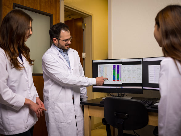 Three researchers looking at results on a computer together, one pointing at charts