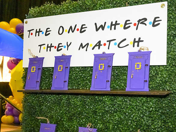 Purple door reveal items on stand with sign that reads, "The One Where They Match."
