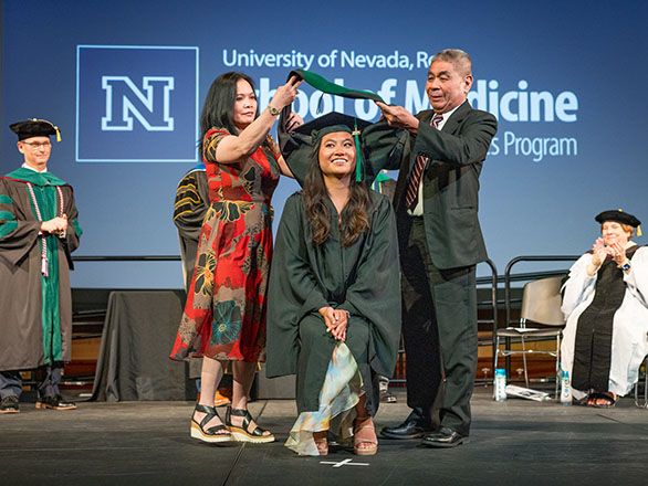 A PA graduate being hooded by their parents.